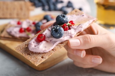 Woman holding tasty cracker sandwich with cream cheese, blueberries, red currants and thyme at table, closeup