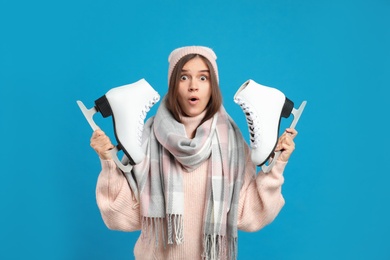 Emotional woman with ice skates on light blue background