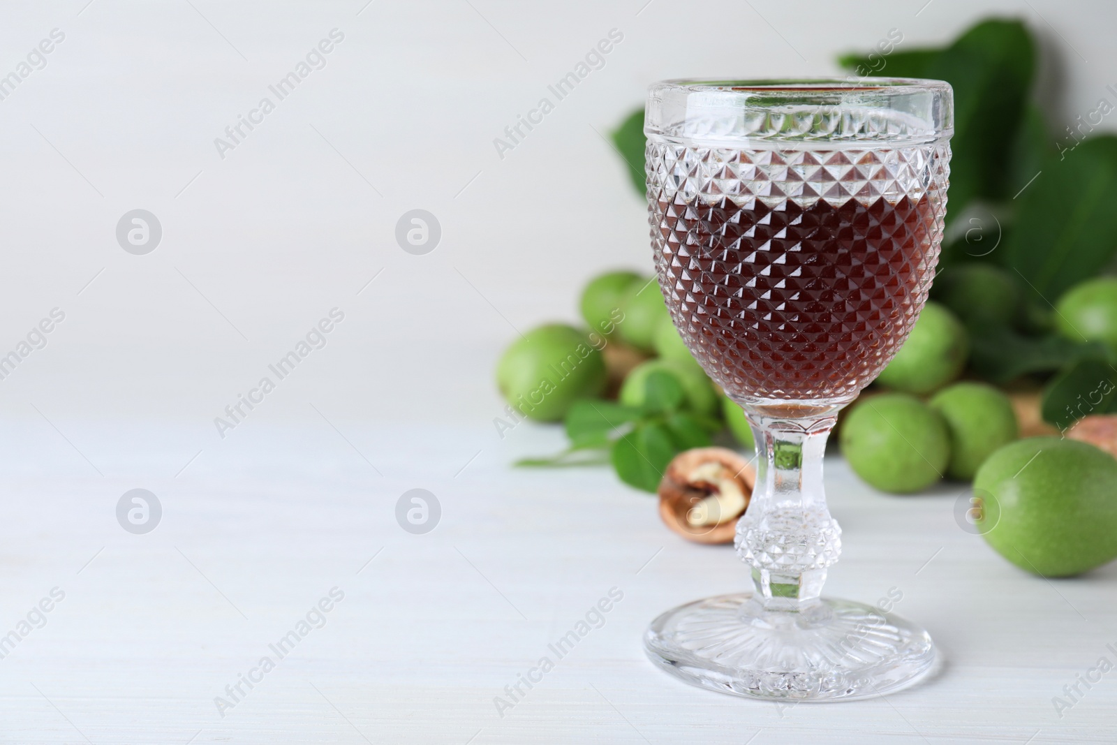 Photo of Delicious liqueur and fresh walnuts on white wooden table, space for text