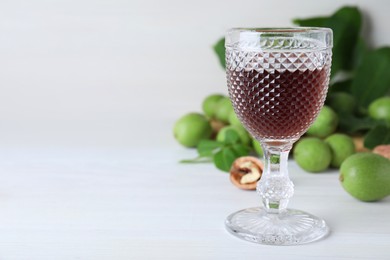 Photo of Delicious liqueur and fresh walnuts on white wooden table, space for text