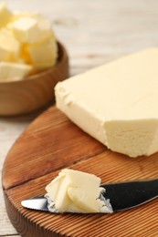 Photo of Tasty butter and knife on light wooden table, closeup