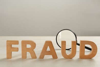 Photo of Word Fraud made of wooden letters and magnifying glass on white table, space for text