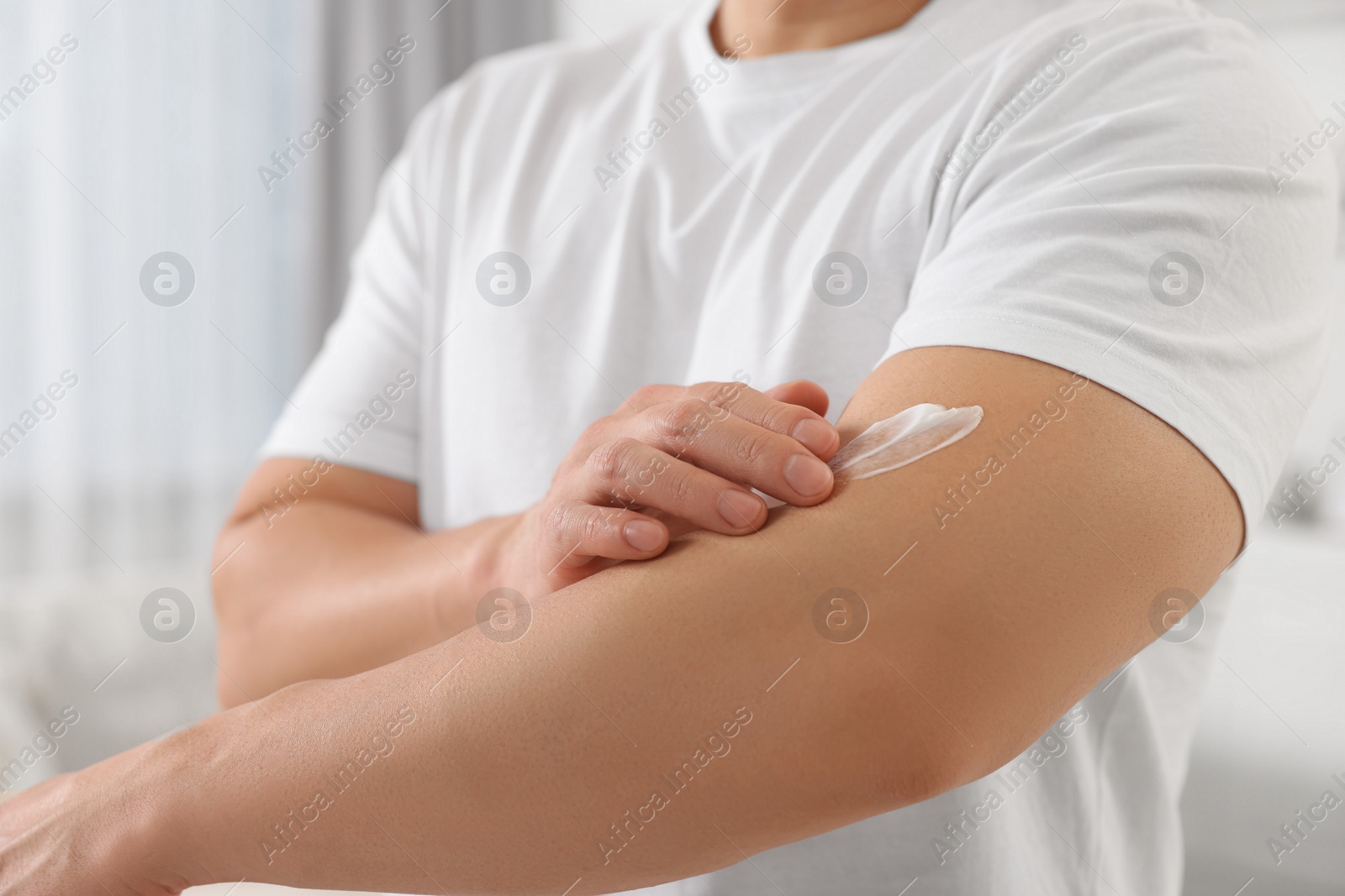 Photo of Man applying body cream onto his arm indoors, closeup