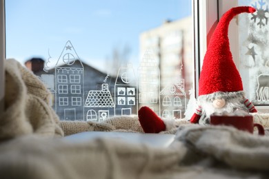 Photo of Gnome and laptop on knitted plaid near window with beautiful drawing at home. Christmas decor