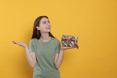 Photo of Portrait of emotional young woman with gift box on yellow background. Space for text