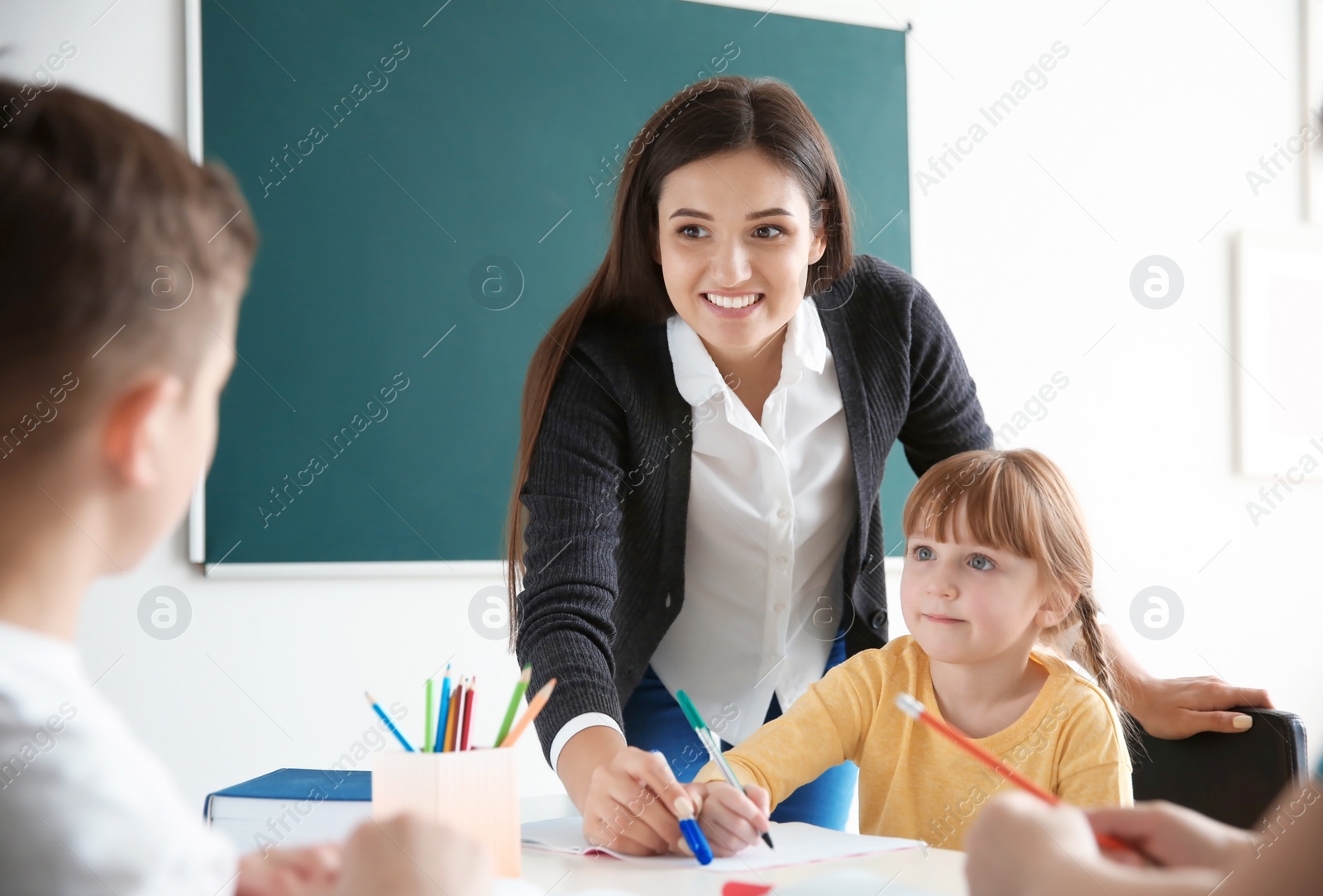 Photo of Female teacher helping girl with her task in classroom at school