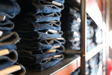 Photo of Collection of modern jeans on shelf in shop, closeup