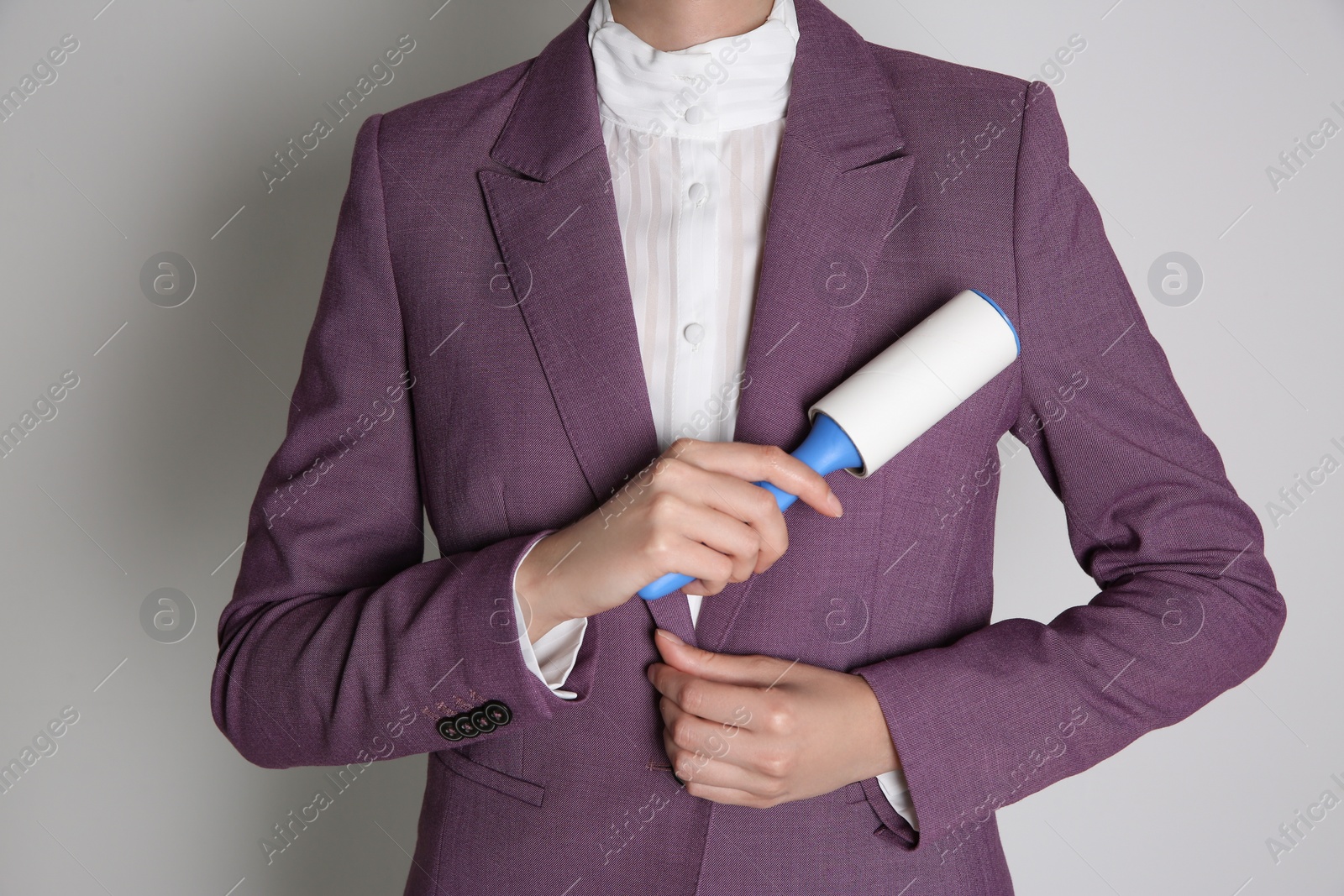 Photo of Woman cleaning purple jacket with lint roller on light grey background, closeup