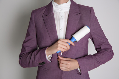 Woman cleaning purple jacket with lint roller on light grey background, closeup