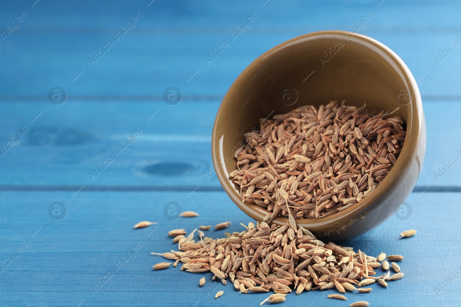 Photo of Overturned bowl with caraway seeds on blue wooden table, space for text
