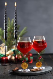 Photo of Christmas Sangria cocktail in glasses and burning candles on dark wooden table