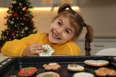 Cute little girl with freshly baked Christmas gingerbread cookie at table indoors