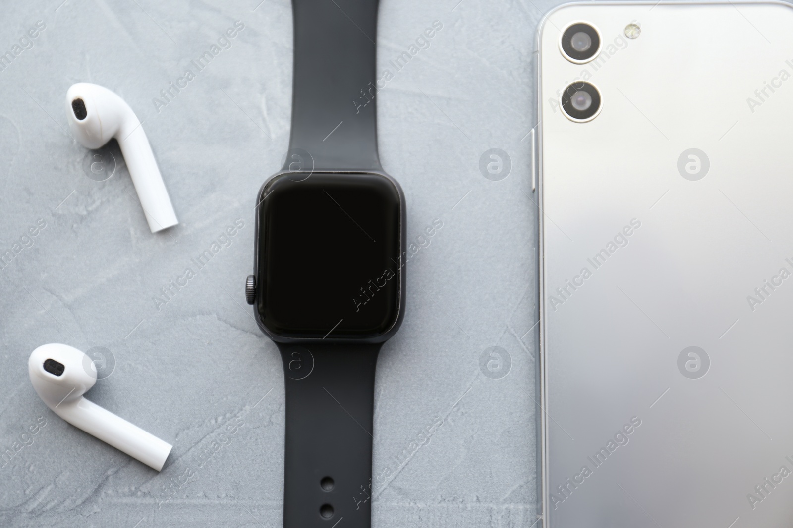 Stylish smart watch, phone and earphones on grey stone table, flat lay Photo of Stylish smart watch, phone and earphones on grey stone table, flat lay