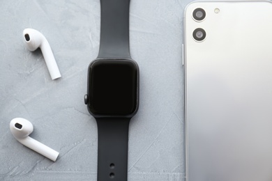 Photo of Stylish smart watch, phone and earphones on grey stone table, flat lay