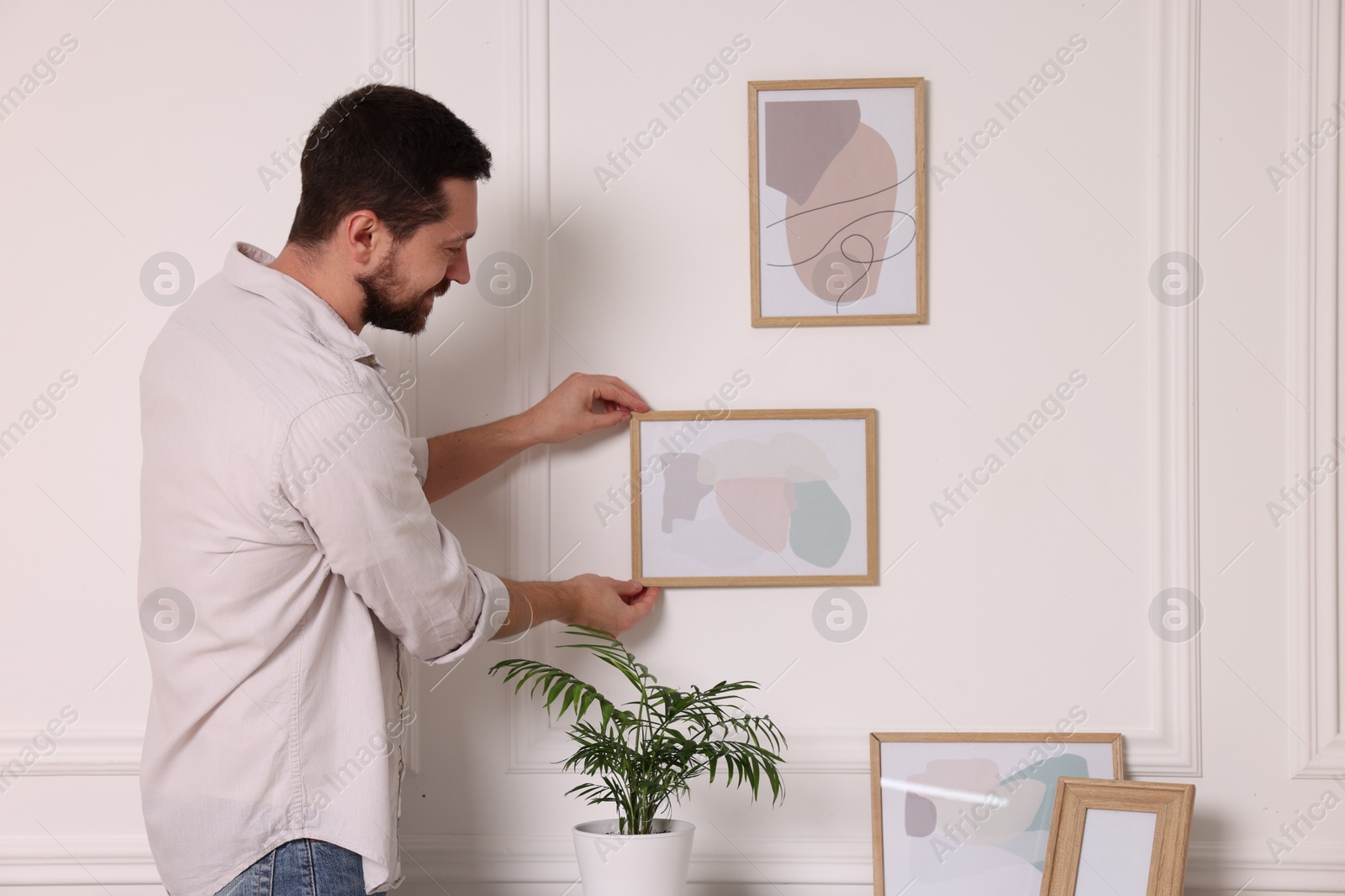 Photo of Man hanging picture frame on white wall at home