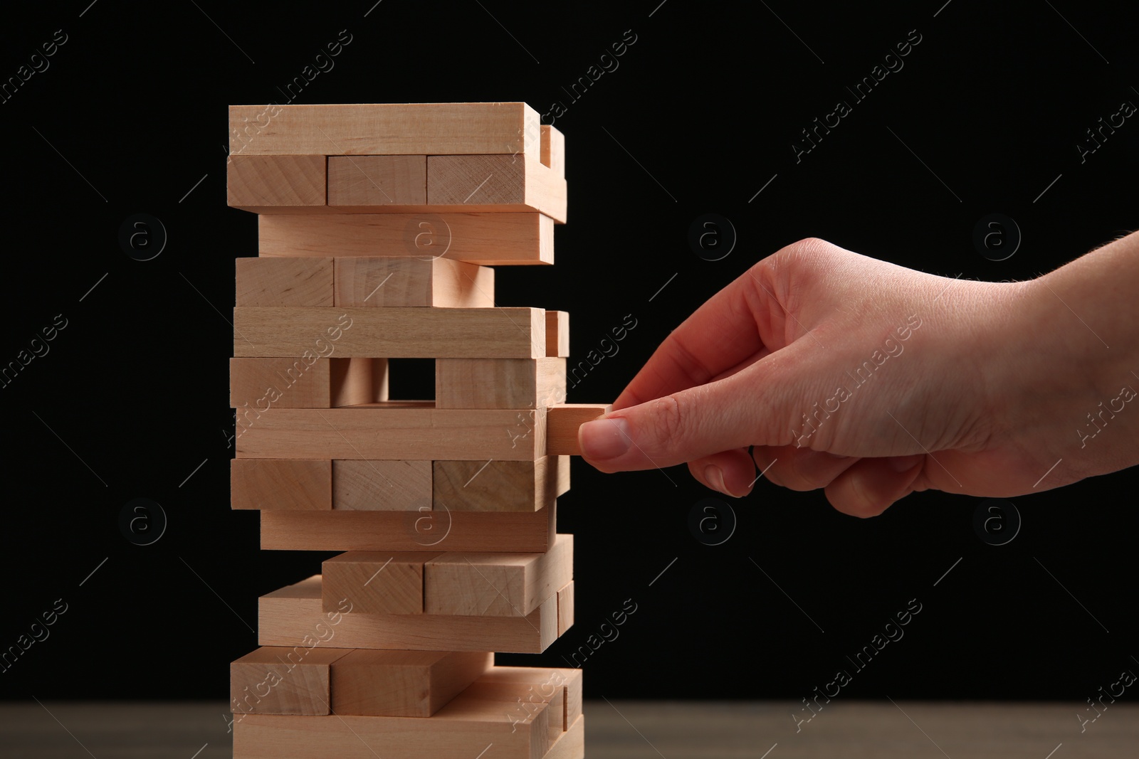 Photo of Woman playing Jenga at table against black background, closeup