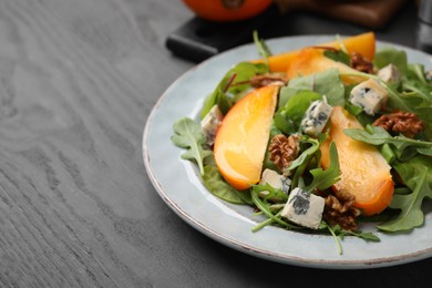 Photo of Tasty salad with persimmon, blue cheese and walnuts served on grey wooden table, closeup. Space for text