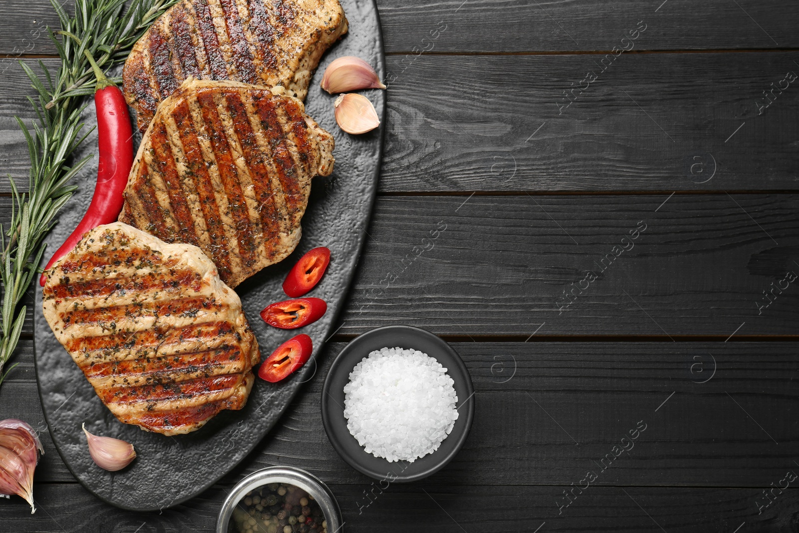 Photo of Delicious grilled pork steaks with spices on dark wooden table, flat lay. Space for text