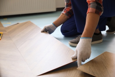 Photo of Worker installing laminated wooden floor indoors, closeup