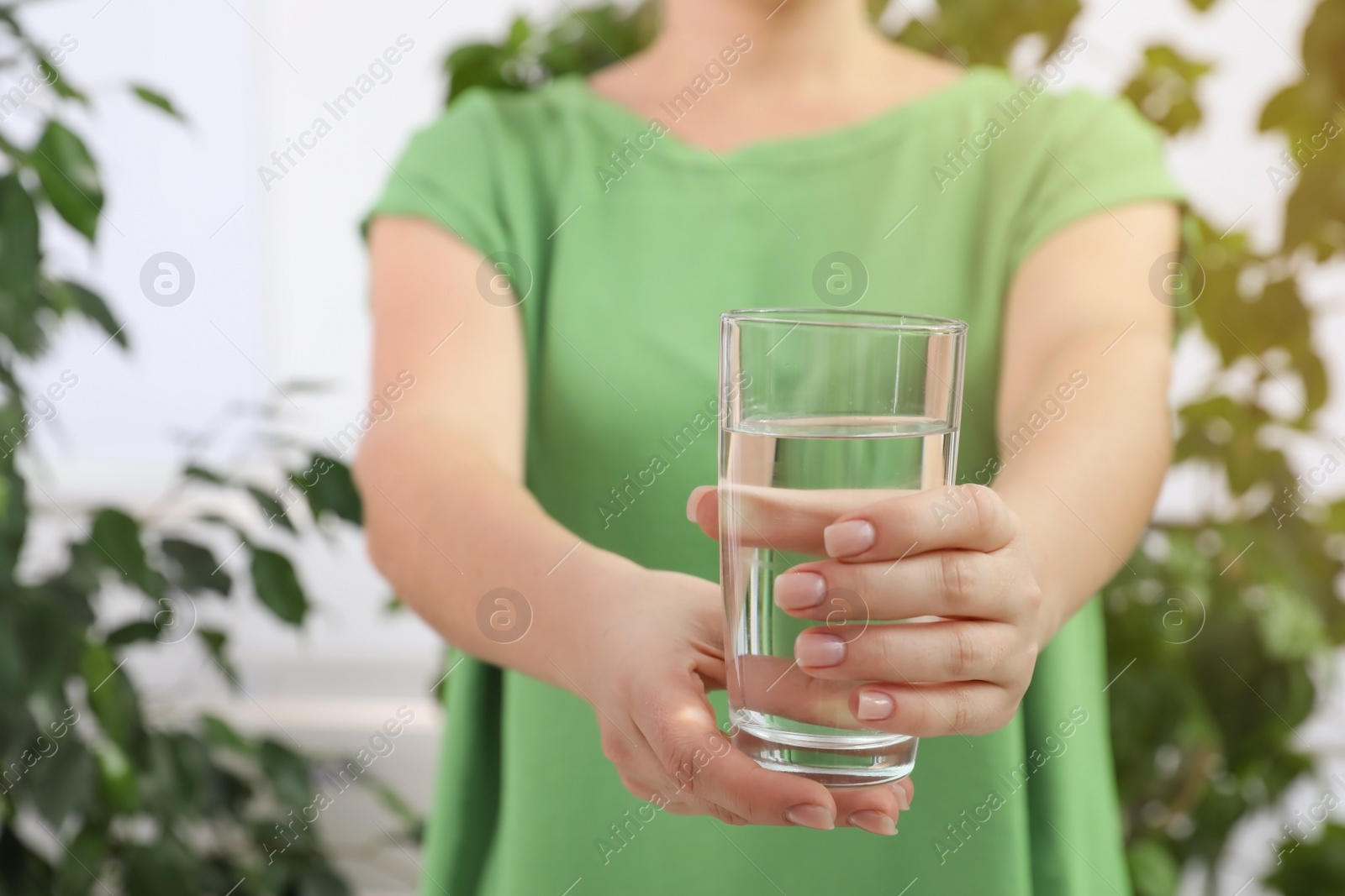 Photo of Woman holding glass of fresh water indoors, closeup