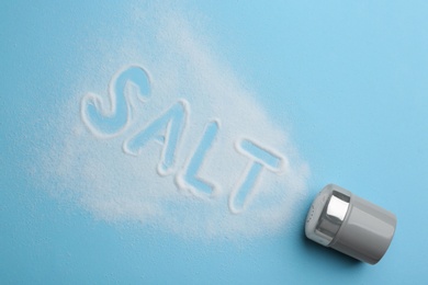 Photo of Word SALT and shaker on light blue background, flat lay