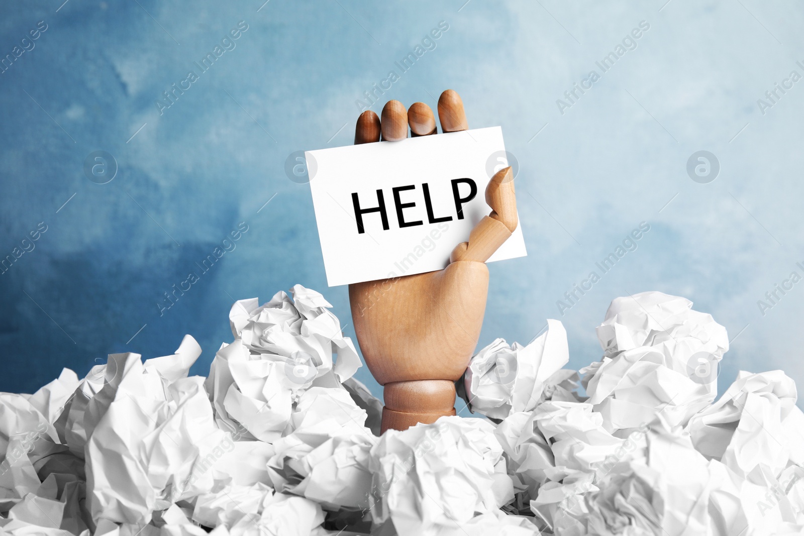 Photo of Wooden hand holding card with word "HELP" among crumpled paper against color background