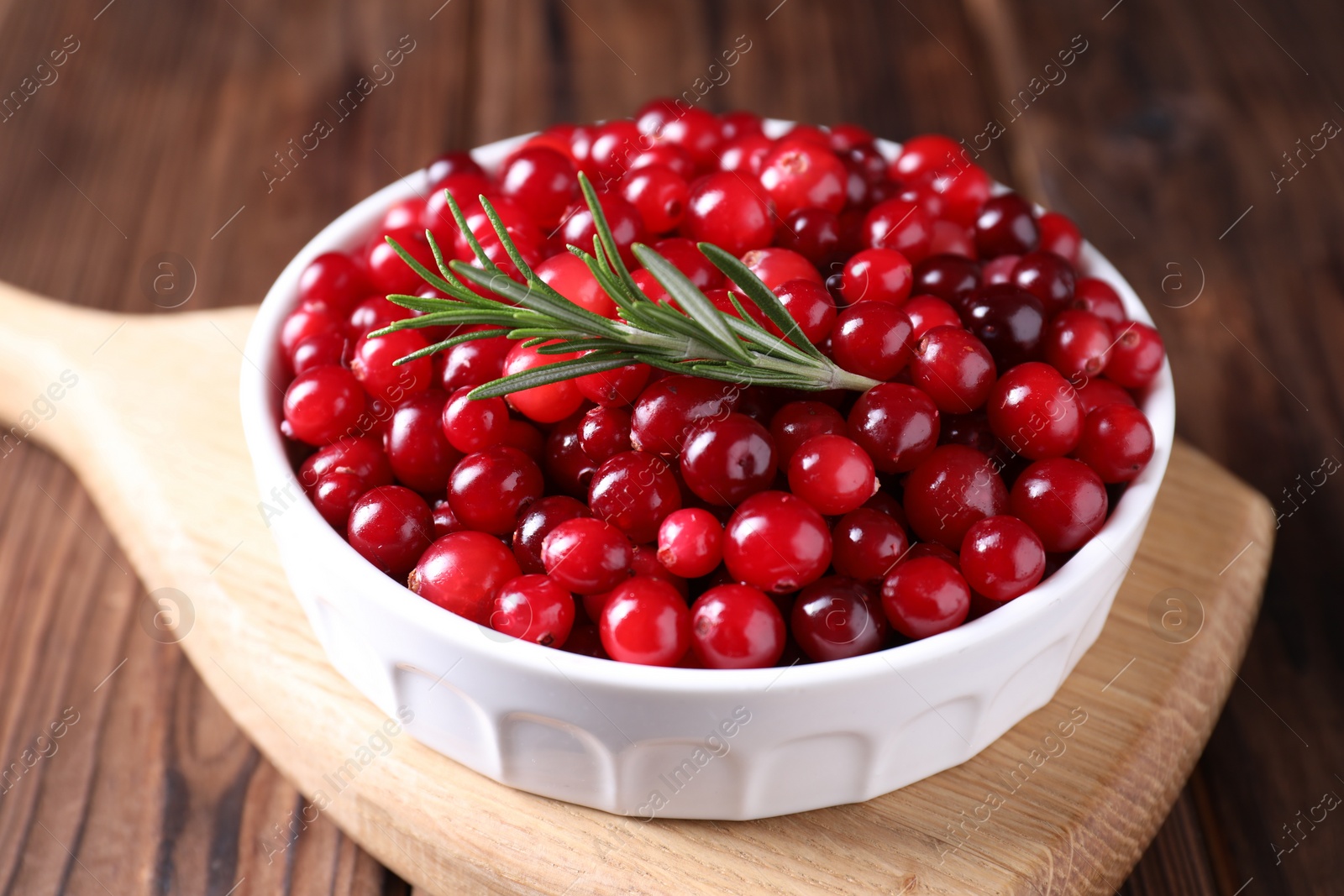 Photo of Fresh ripe cranberries and rosemary in bowl on wooden table, closeup