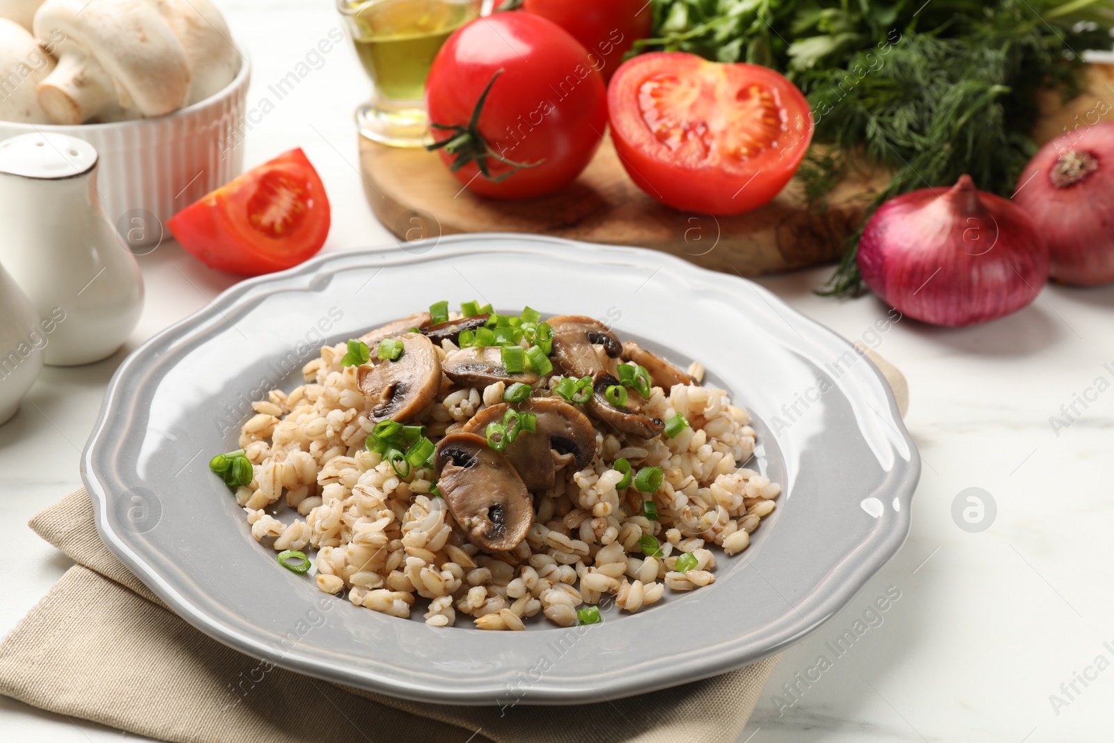 Photo of Delicious pearl barley with onion and mushrooms served on white table