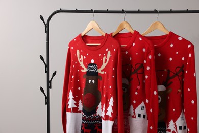 Different Christmas sweaters hanging on rack against light background