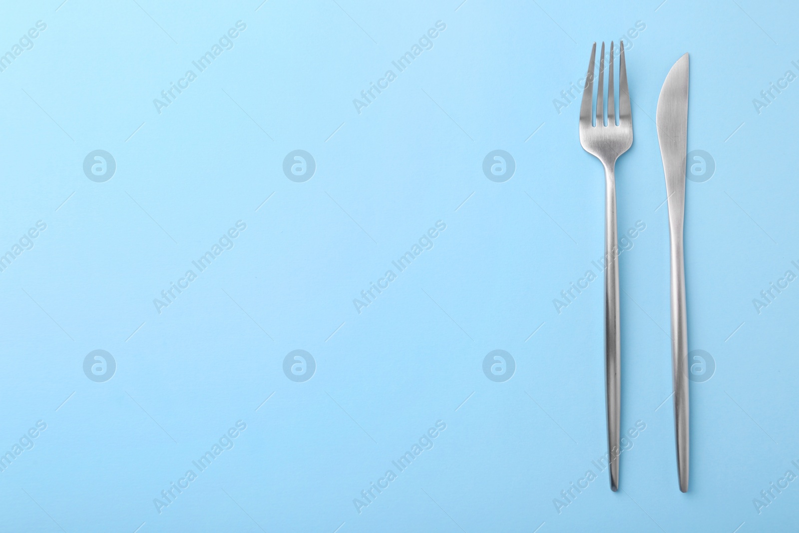 Photo of Stylish cutlery on light blue table, top view. Space for text