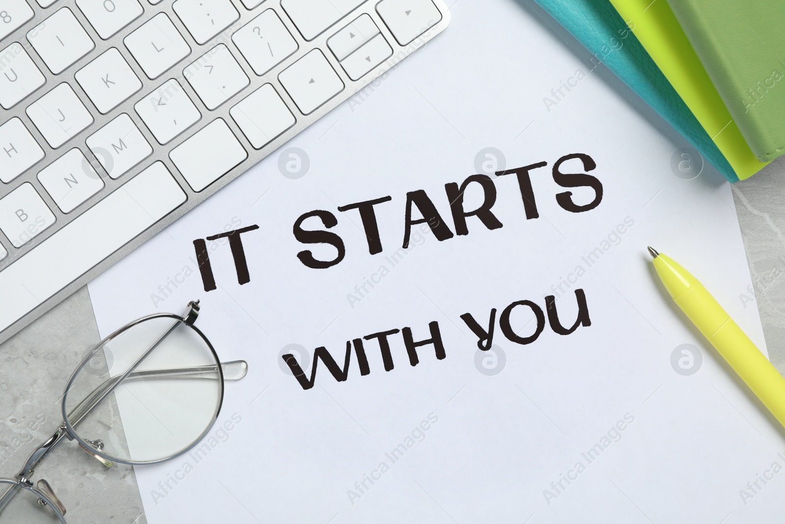 Photo of Sheet of paper with phrase It Starts With You, keyboard and stationery on grey table, flat lay