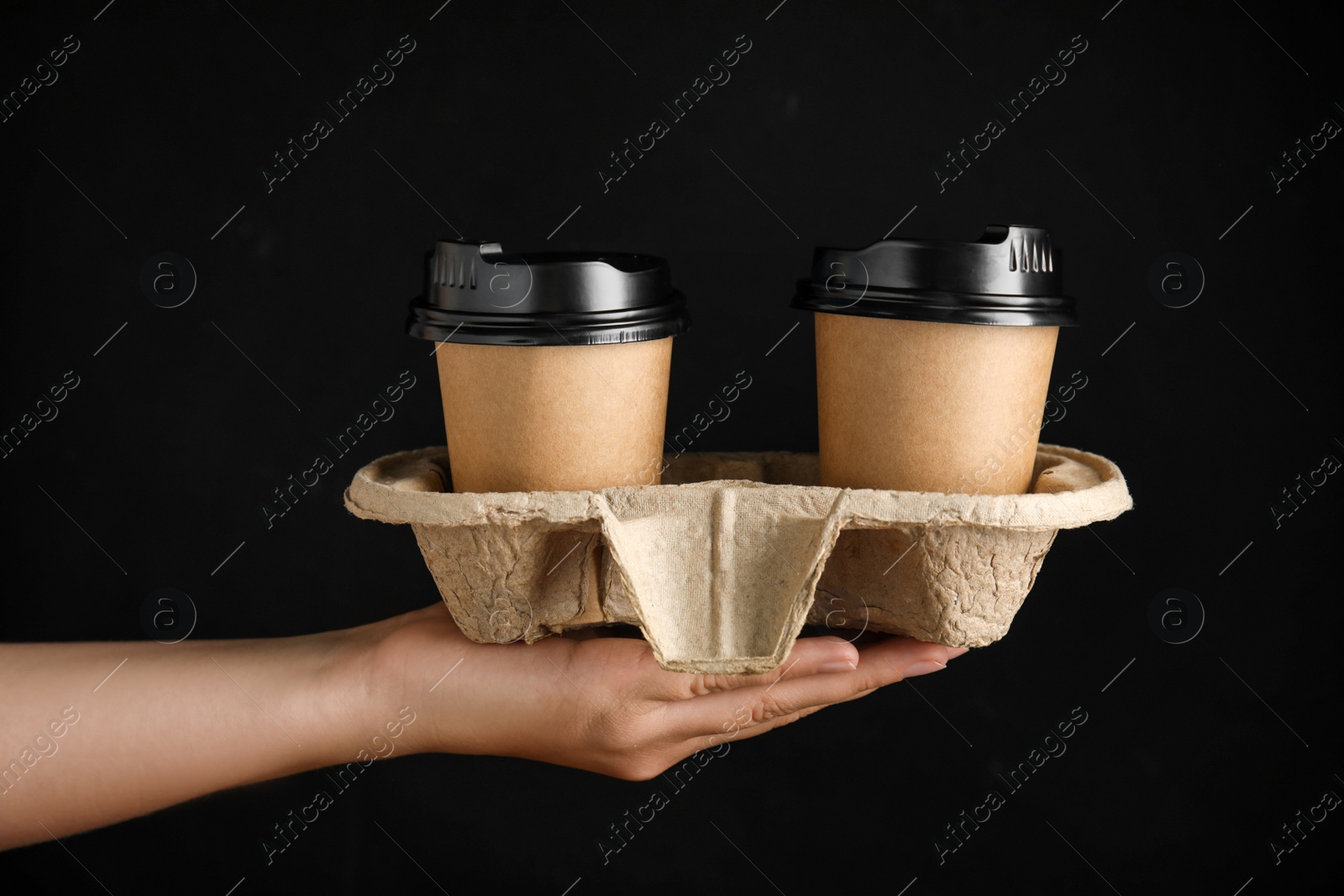 Photo of Woman holding cardboard holder with takeaway paper coffee cups on black background, closeup