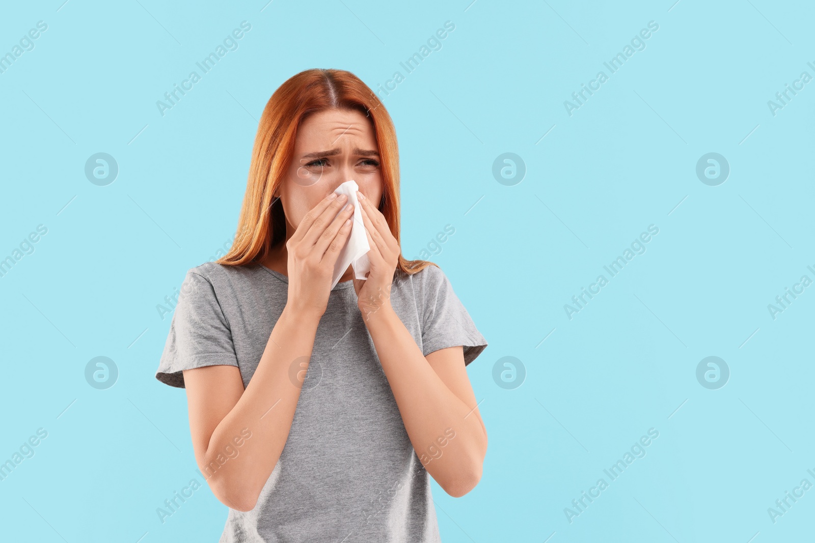 Photo of Suffering from allergy. Young woman with tissue sneezing on light blue background, space for text