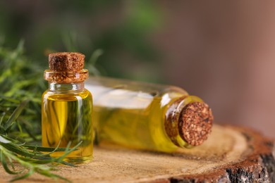 Photo of Bottles of essential oil and fresh tarragon leaves on wooden stump, closeup