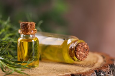 Bottles of essential oil and fresh tarragon leaves on wooden stump, closeup