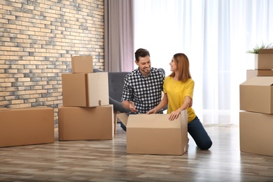 Photo of Couple unpacking cardboard box in their new house. Moving day