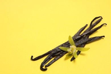 Photo of Vanilla pods and beautiful flower on yellow background. Space for text