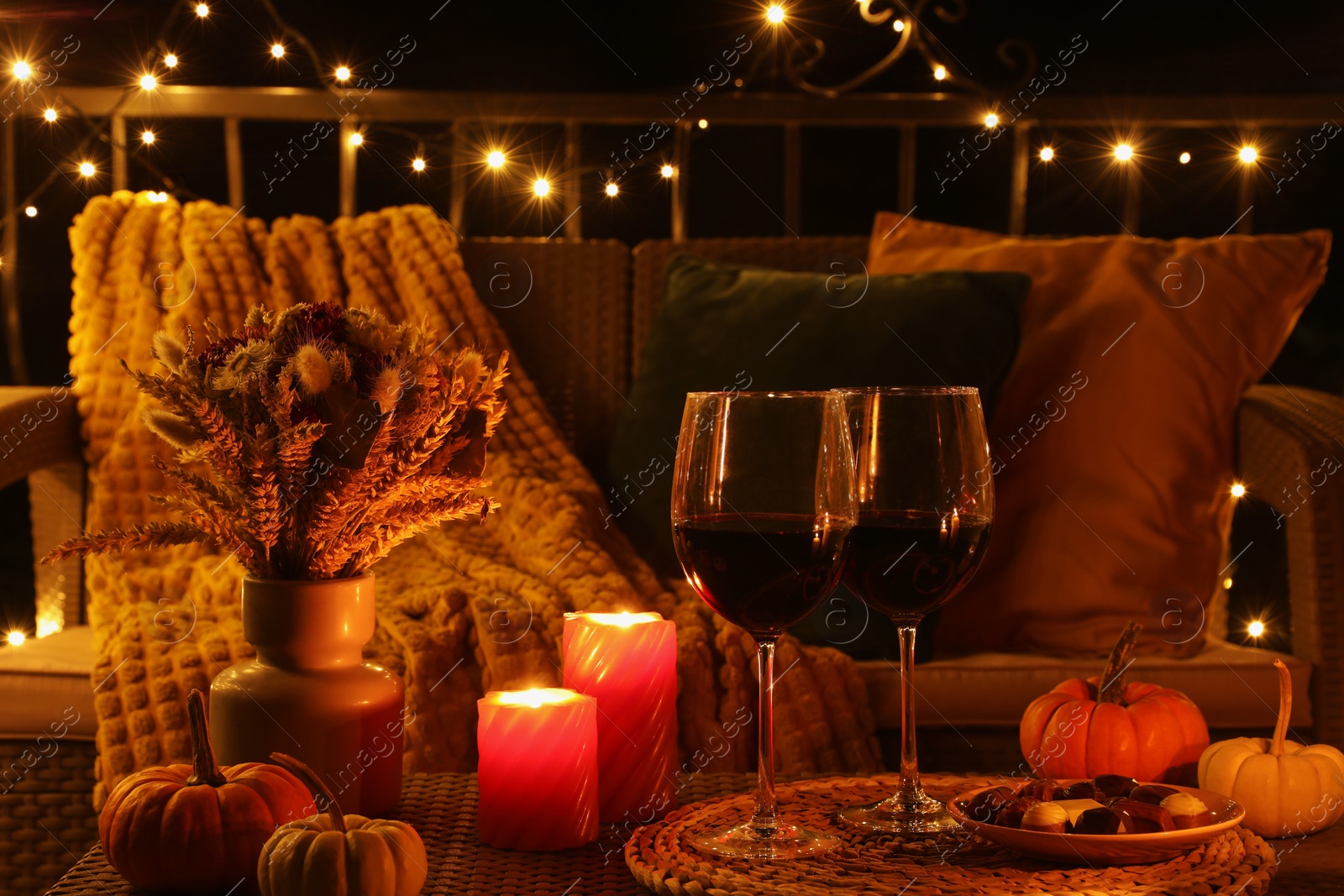 Photo of Glasses of wine, burning candles and autumn decor on outdoor terrace in evening