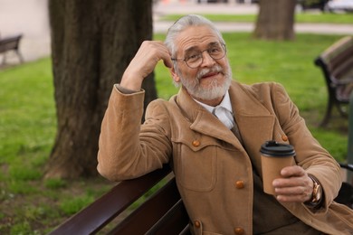 Photo of Handsome senior man sitting on bench and drinking coffee outdoors, space for text