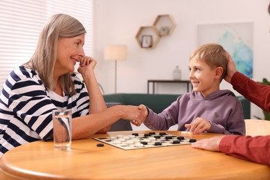Photo of Family playing checkers in room. Grandmother shaking hands with her nephew after game
