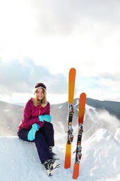 Photo of Young woman with ski equipment sitting on snowdrift in mountains. Winter vacation