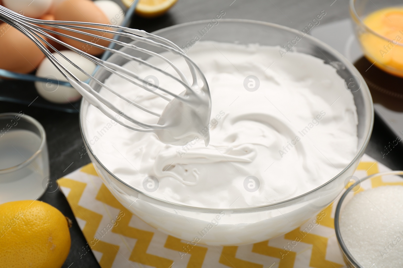 Photo of Bowl with whipped cream, whisk and ingredients on table, closeup