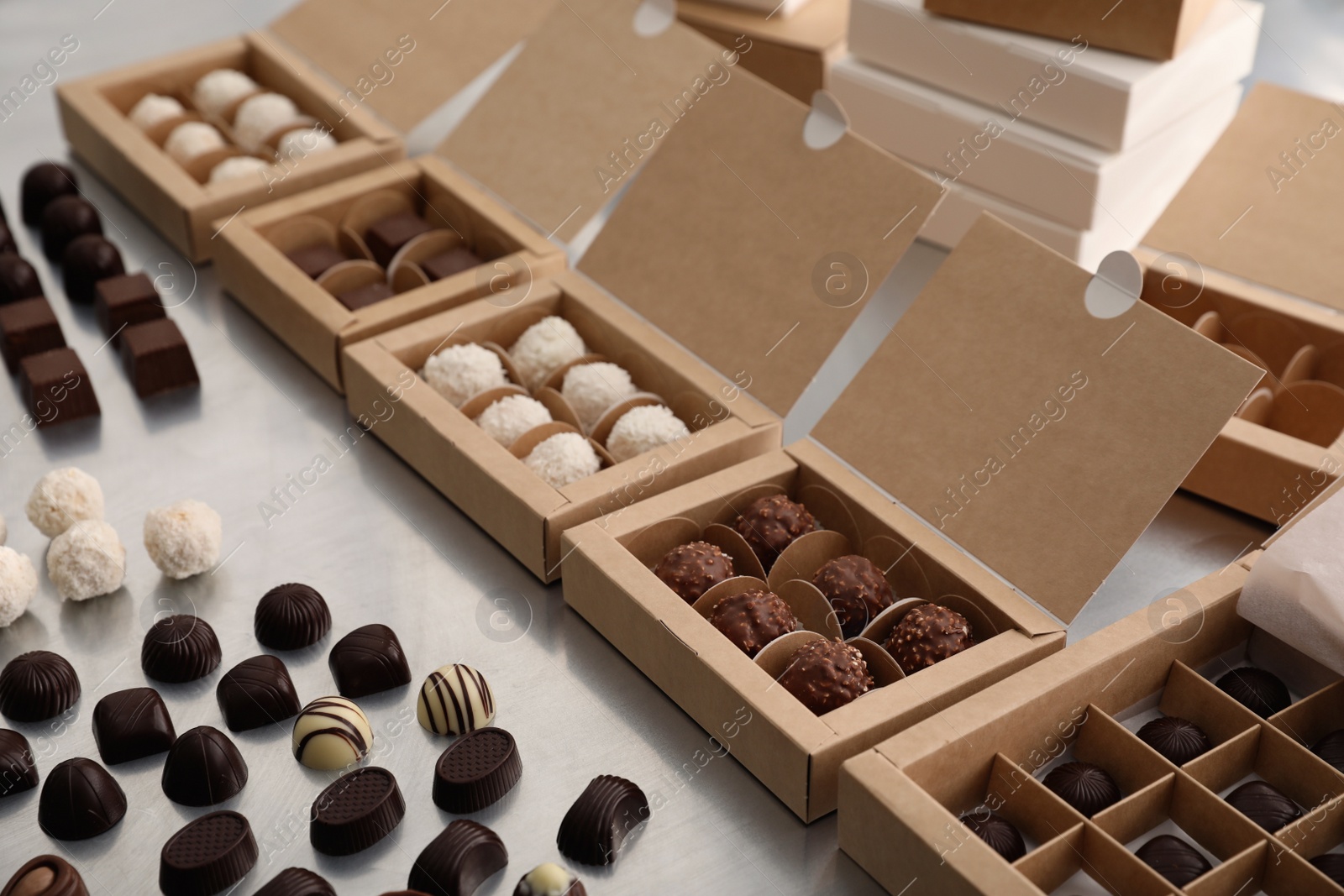 Photo of Different delicious chocolate candies and boxes on white table. Production line