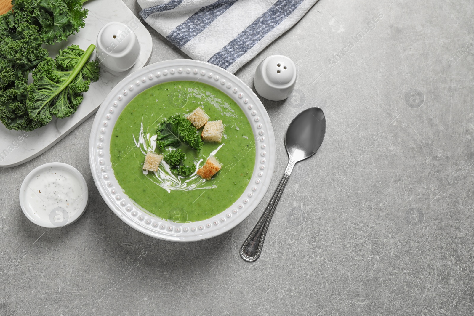 Photo of Tasty kale soup with croutons served on grey table, flat lay