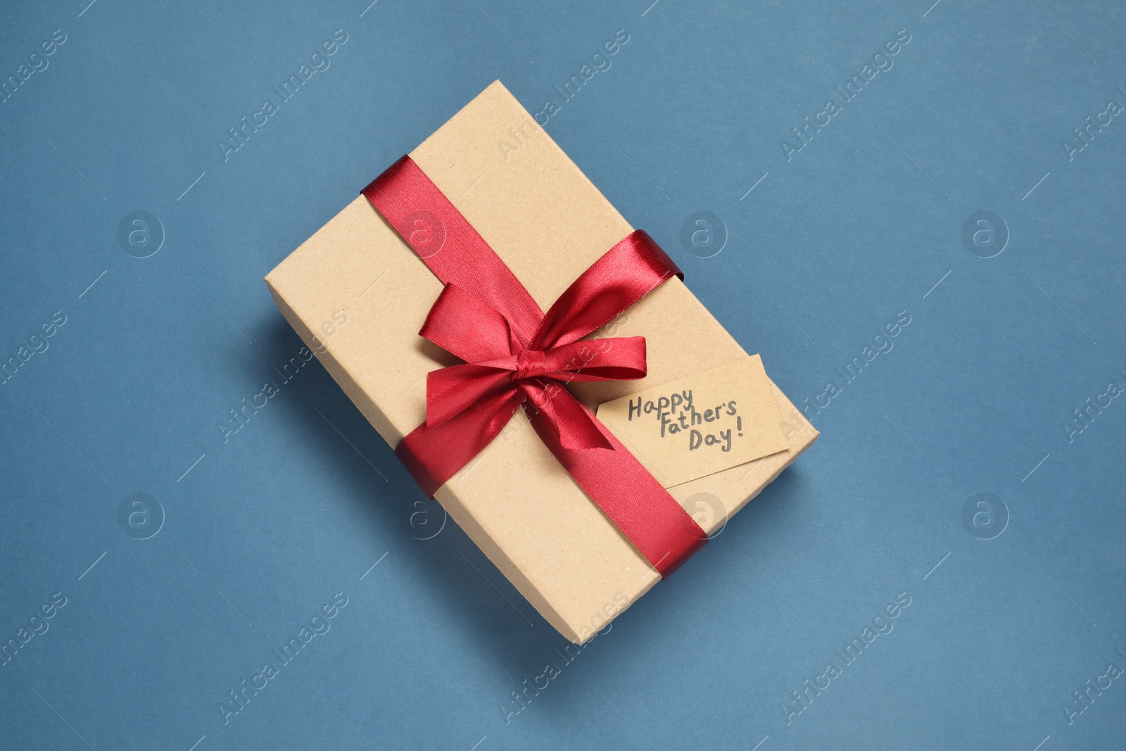 Photo of Card with phrase Happy Father's Day and gift box on blue background, top view