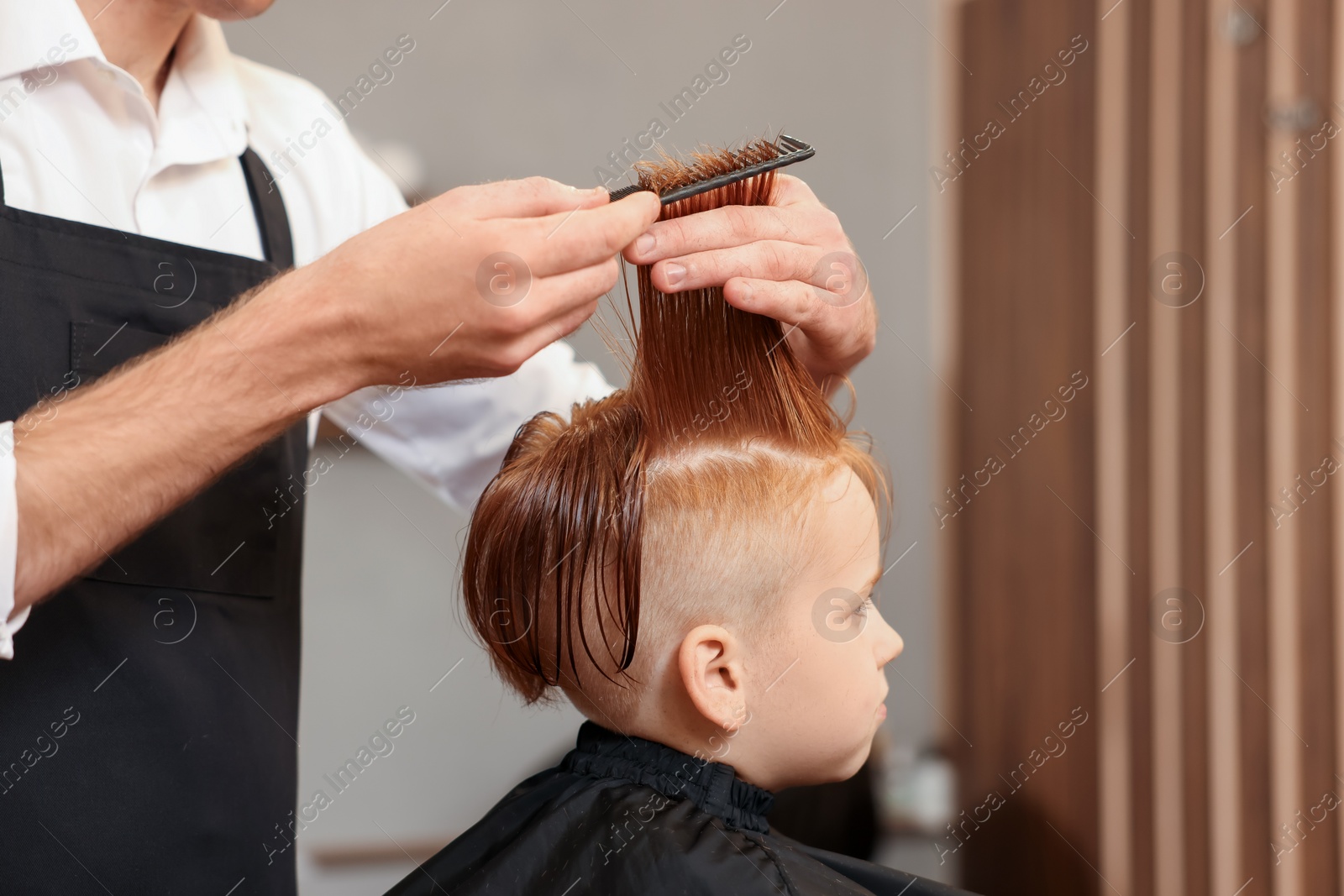 Photo of Professional hairdresser combing boy's hair in beauty salon, closeup