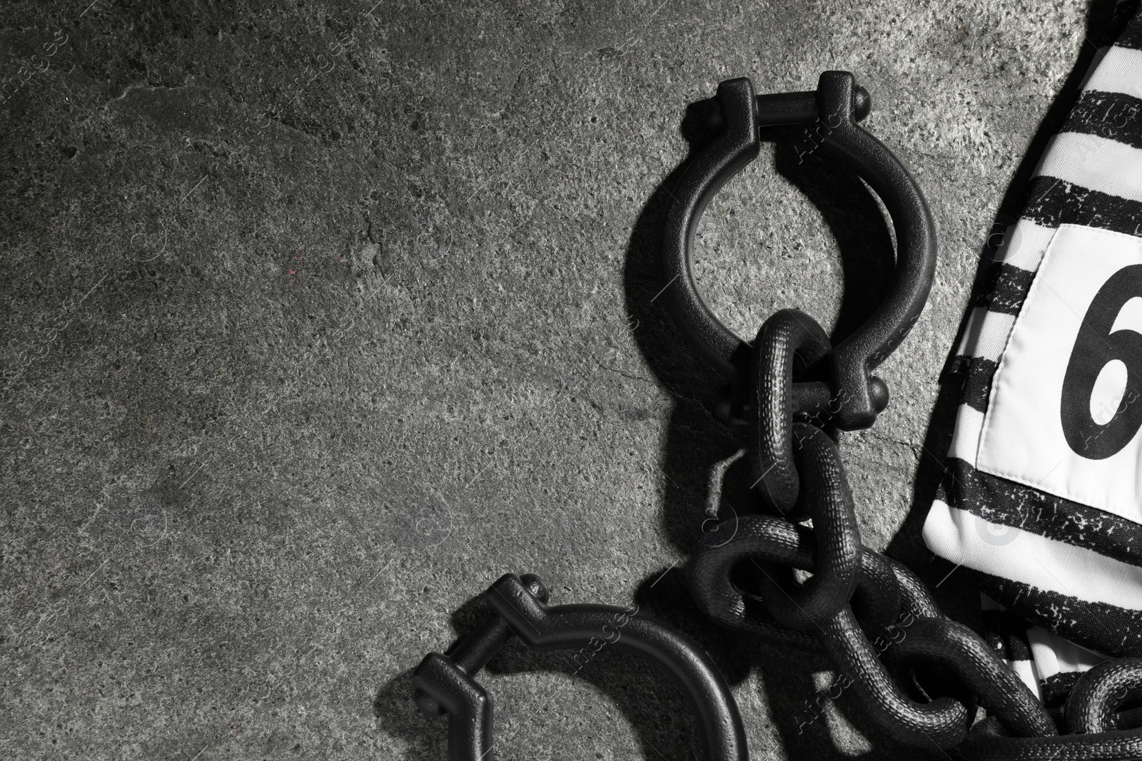 Photo of Steel shackles and jail clothes on grey table, flat lay. Space for text