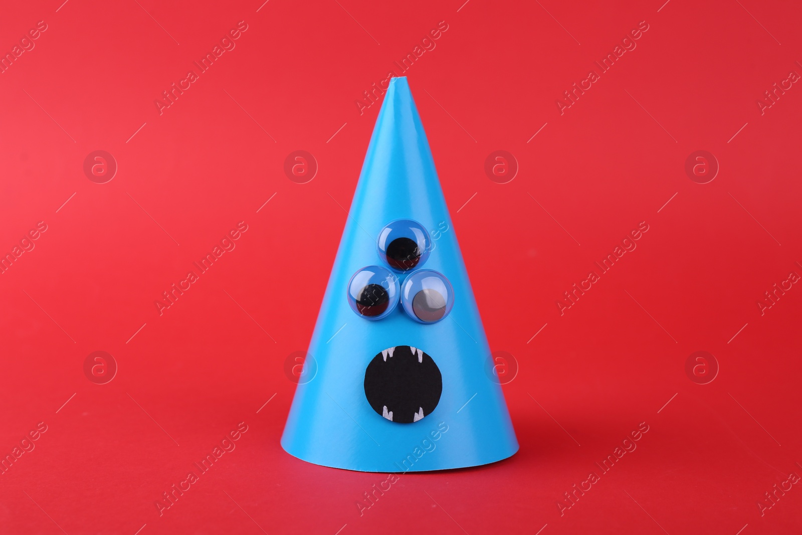 Photo of Monster made of light blue paper on red background. Halloween decoration