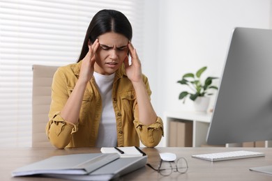 Photo of Young woman suffering from headache at wooden table in office