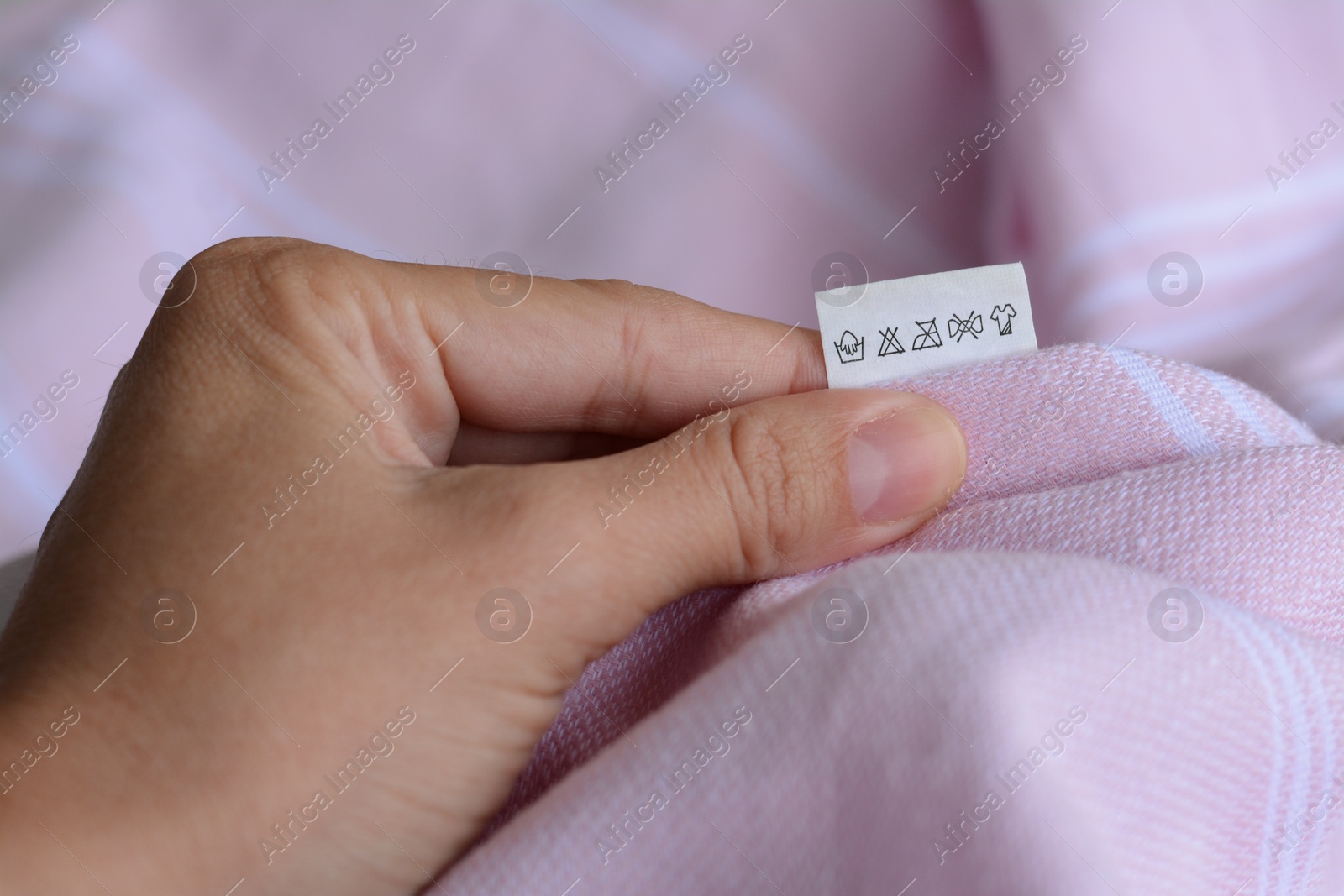 Photo of Woman holding white clothing label on pale pink garment, closeup